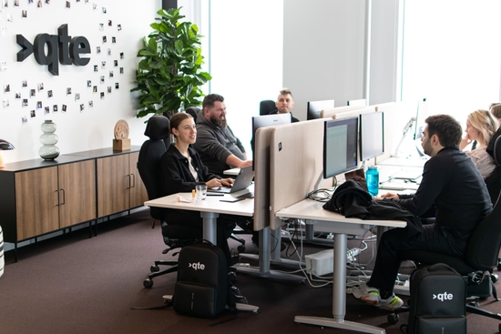 En grupp medarbetare på qte sitter vid sina skrivbord och arbetar.